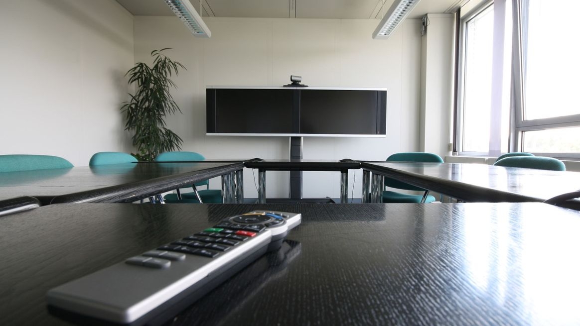 Ein leerer Besprechungsraum in einem Unternehmen, der für Videokonferenzen mit einem Doppelbildschirm, Kamera und Fernbedienung ausgestattet ist.