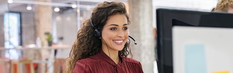 Eine Frau sitzt mit Headset an einem Computer-Arbeitsplatz.