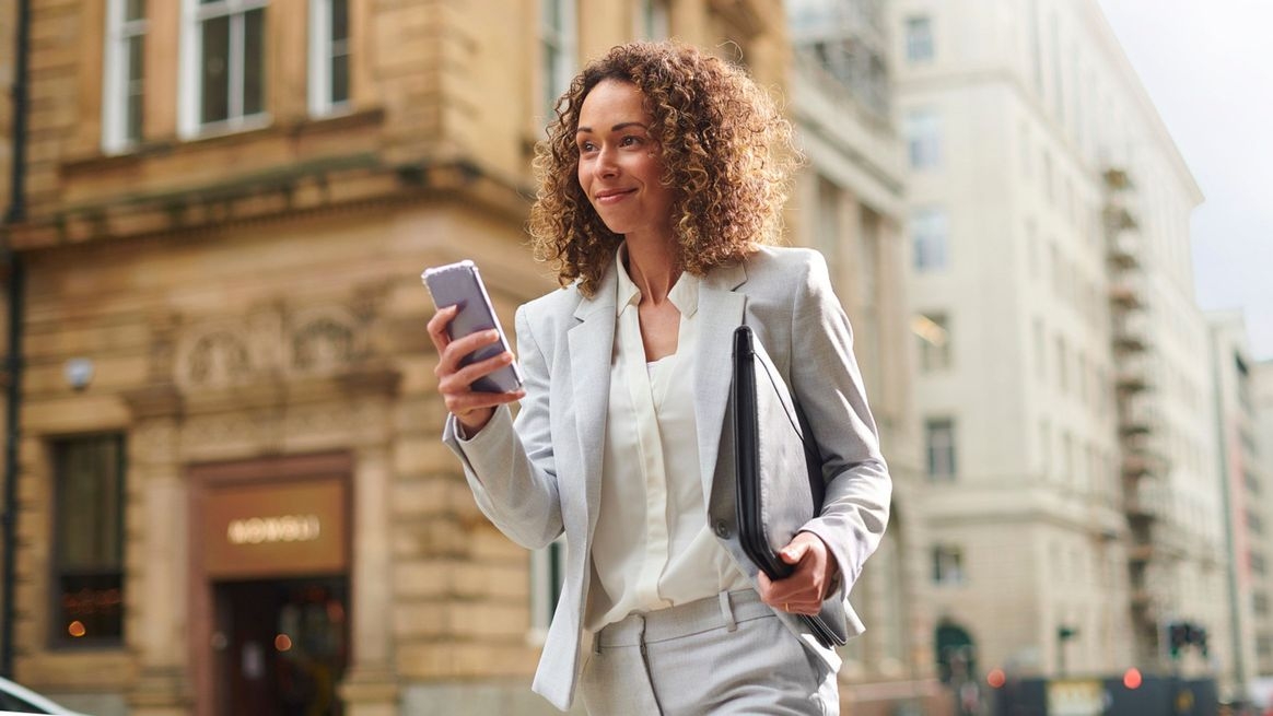 Eine junge Frau in einem Kostüm läuft eine Straße entlang und blickt auf ihr Smartphone.