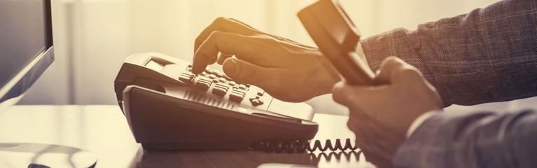 Eine Hand tippt auf die Tastatur eines stationären Telefons