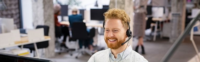 Glücklich wirkender Kundendienst-Mitarbeiter spricht über ein Headset in einem Callcenter