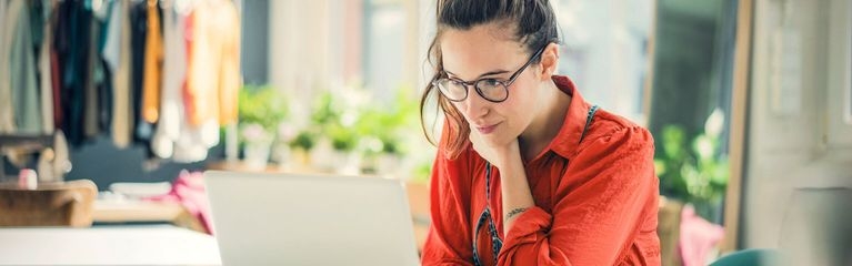 Frau in roter Bluse und mit Brille sitzt am Laptop