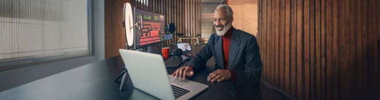 Älterer Herr sitzt am Schreibtisch mit Laptop