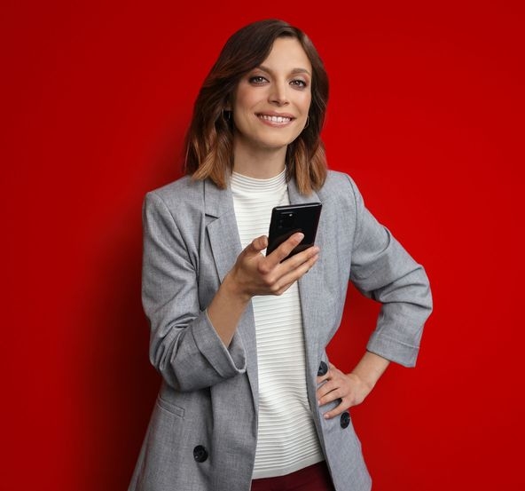 Frau steht mit dem Smartphone in der Hand vor einem roten Hintergrund
