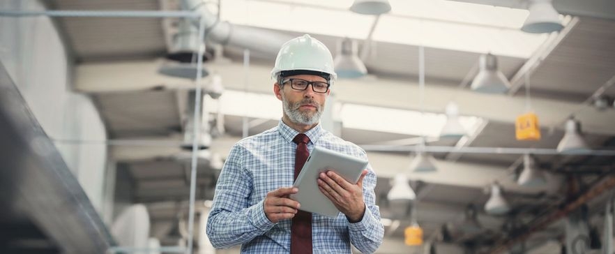 Ein Bauingenieur steht mit seinem Tablet in einer Werkshalle